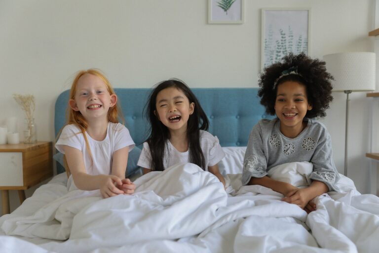 Three little girls giggling in a big bed.