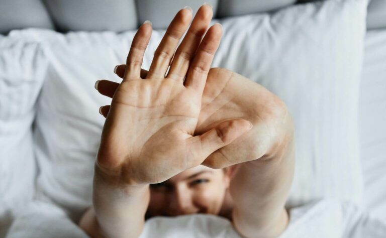 A top view of a woman in bed stretching out her arms as she wakes up from healthy sleep