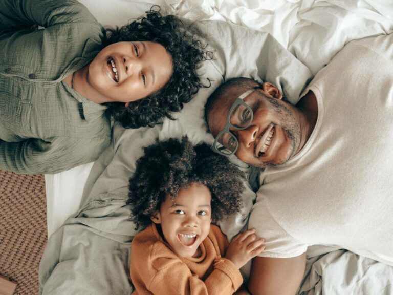 A family of 3 having fun while laying in bed.