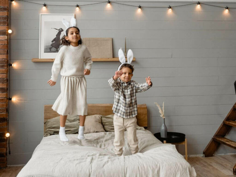 Two young multi racial children jumping on a bed wearing white bunny ears.